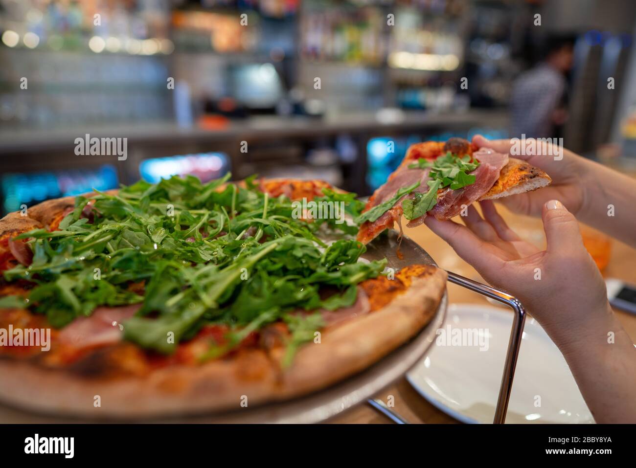 Frau, die eine Scheibe Pizza mit den Arugula-Grüns auf der Oberseite ergreift Stockfoto