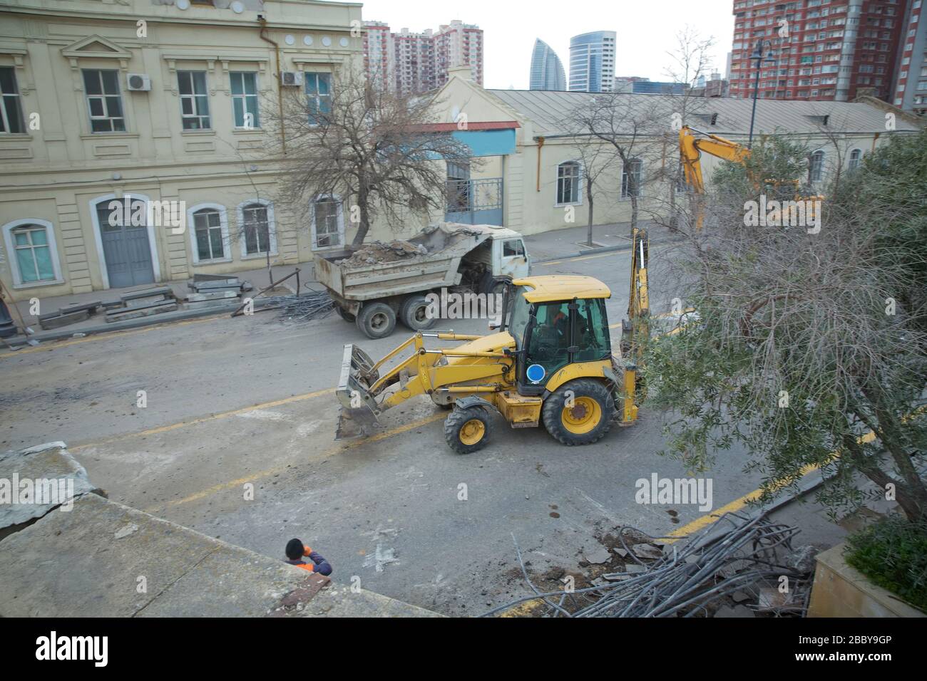 Sie reißen die Brücke ab. Kamaz, mit Steinboden beladen, hielt auf der Straße an. Der gelbe Traktor arbeitet in der Stadt, die Straßenreparatur in der Stadt. Stockfoto