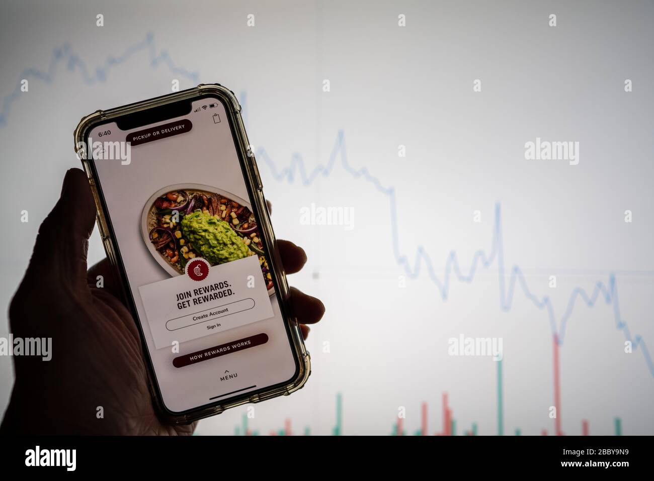 Chipotle Mobile App auf dem iPhone vor der weißen Börsenkarte mit einem Diagramm, das den Wert abgesenkt hat Stockfoto