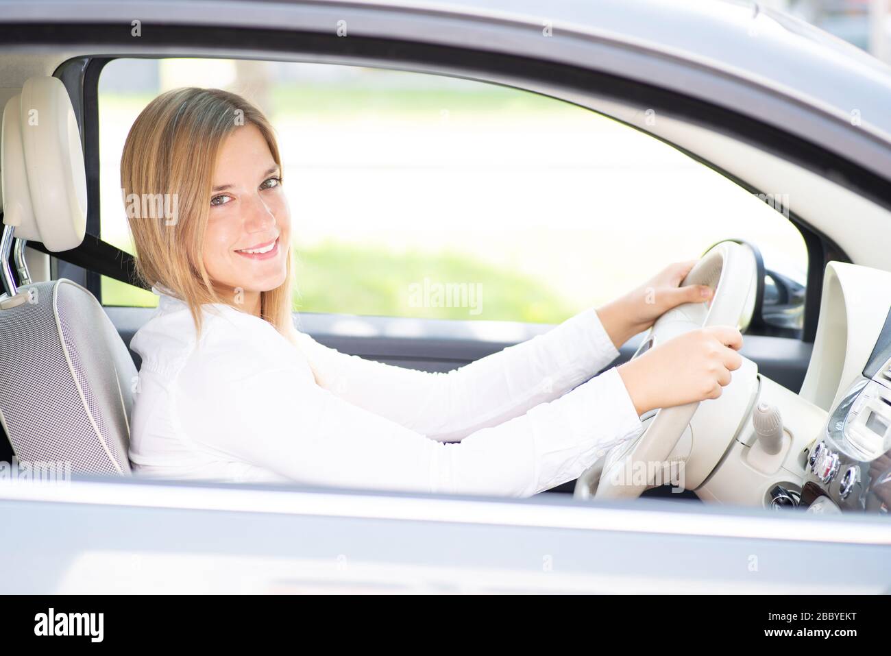 Personable junge Frau mit nettem Lachen sitzt in einem neuen Auto Stockfoto