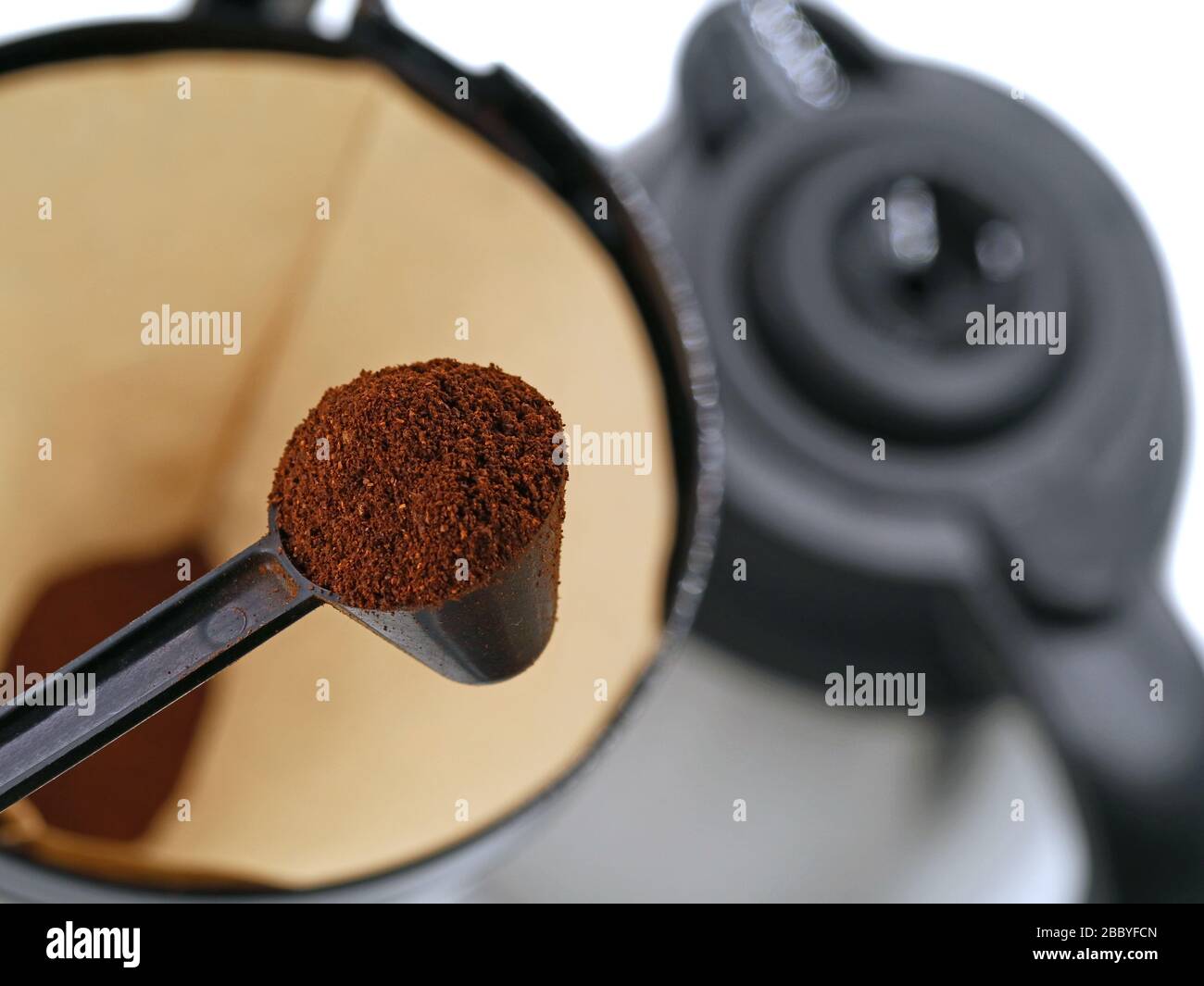 Löffel mit Kaffeepulver vor dem Kaffeesieb mit Kaffeekanne im Hintergrund. Konzept zur Kaffeezubereitung Stockfoto