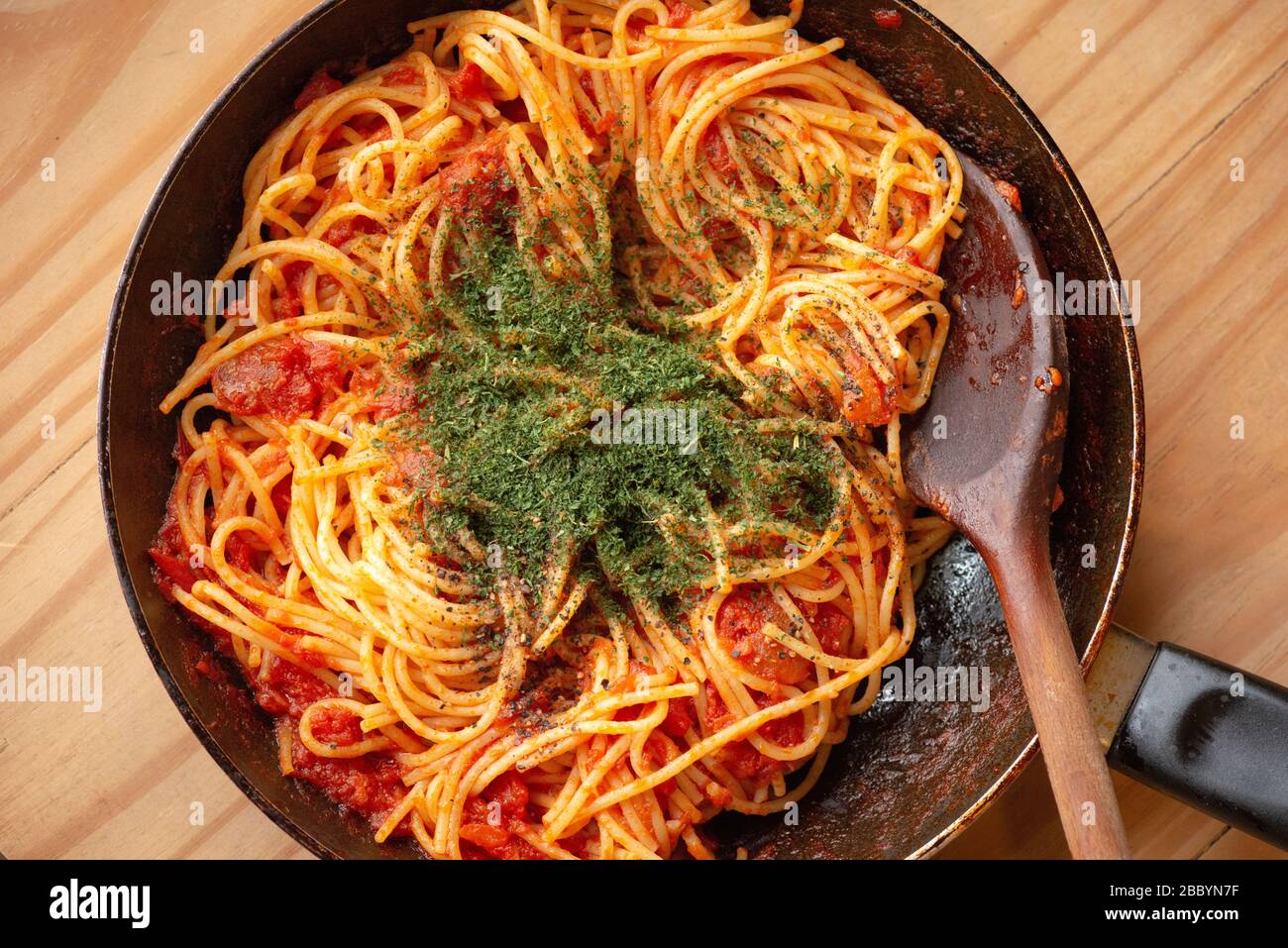 Traditionelle hausgemachte, traditionelle Spaghetti-Pasta in Tomatensauce und Kräuter mit Holzlöffel in rustikaler Bratpfanne. Stockfoto