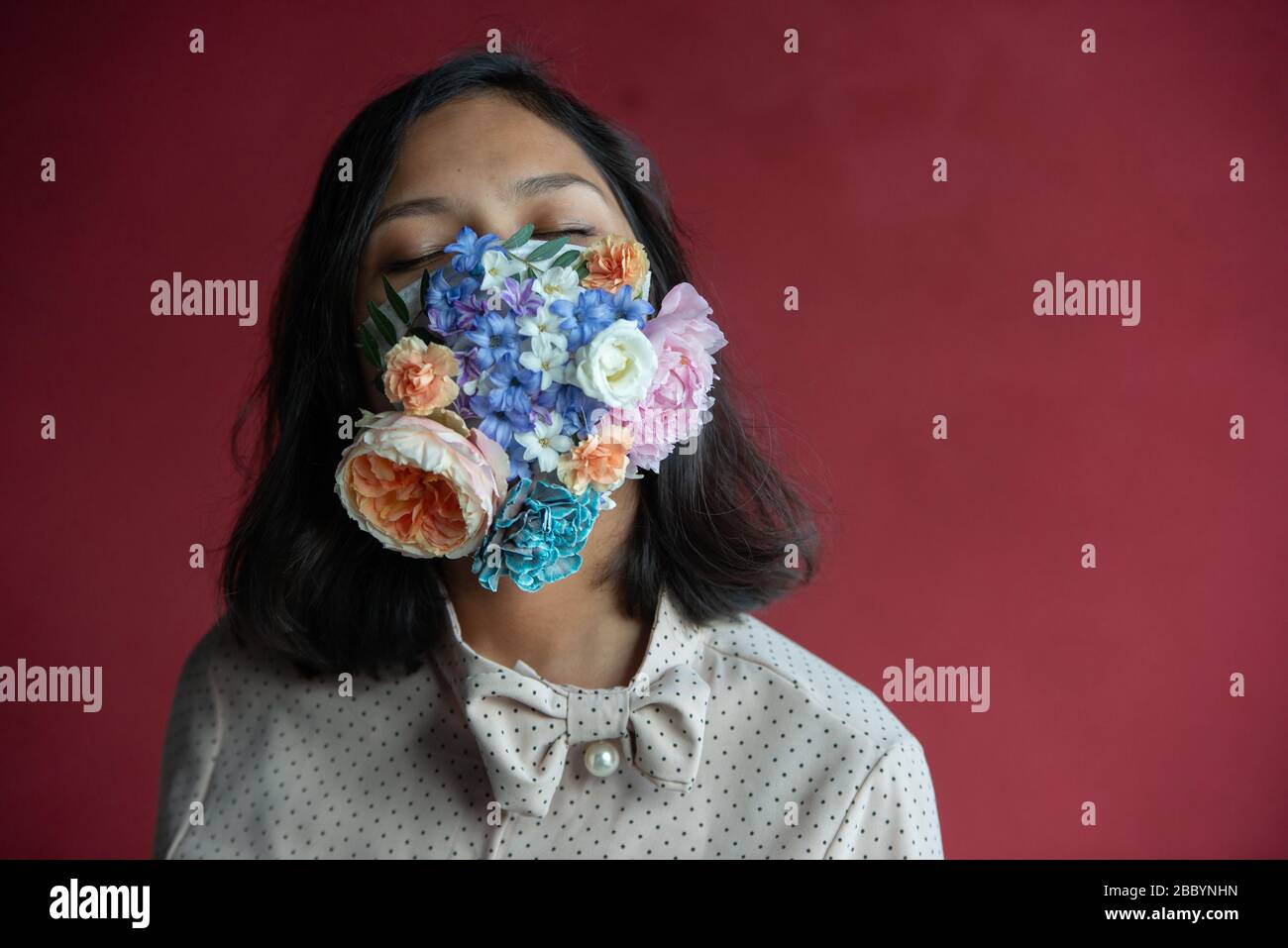 Frau in schützender medizinischer Maske mit Blumen auf rotem Hintergrund. Bündnisschutz -19. Stockfoto