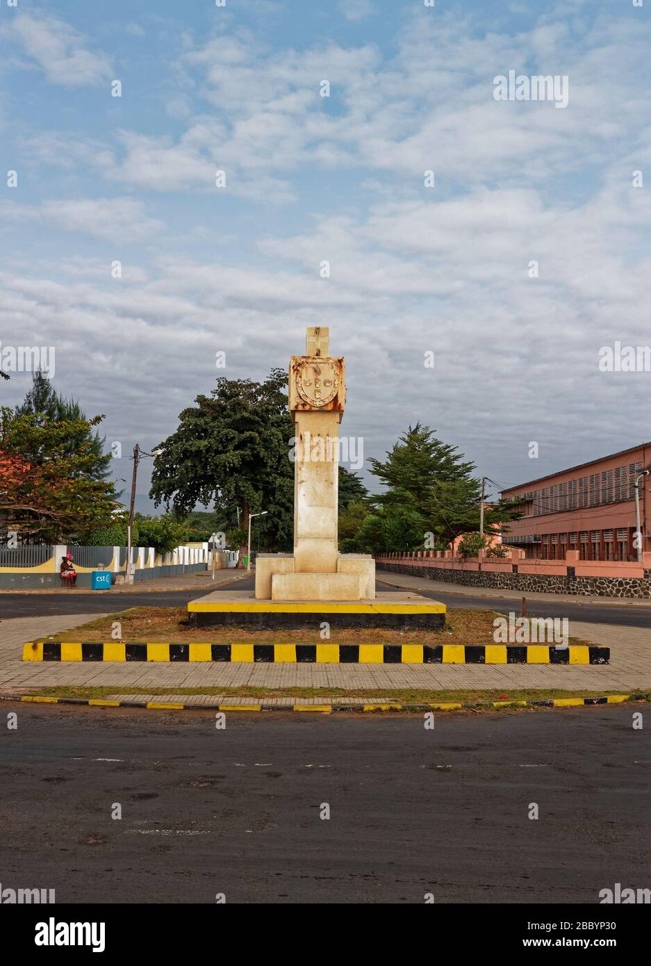 Ein Denkmal im sowjetischen Stil in Sao Tome im Zentrum eines kleinen Kreisverkehrs mit einer von Bäumen gesäumten Allee dahinter. Stockfoto