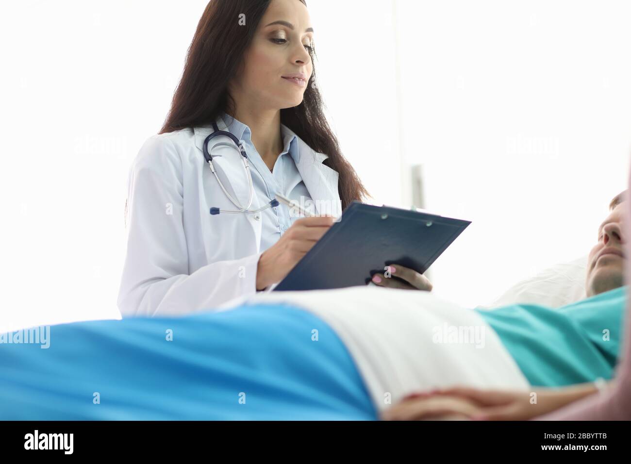 Weiblicher Arzt steht über dem Mann, der ein Krankenhausbett liegt Stockfoto