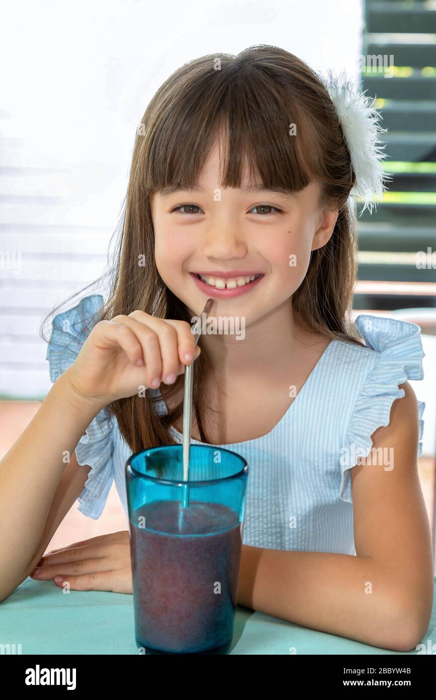 Acht Jahre altes Mädchen trinkt einen Smoothie aus einem Metallstroh Stockfoto