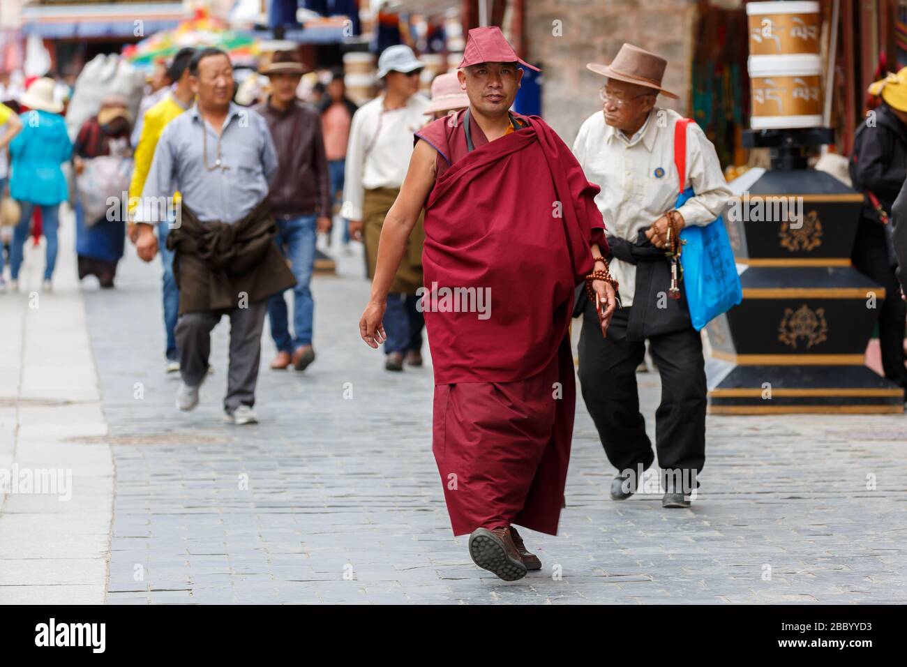 Mönch mittleren Alters in traditionellen Tuch (roter Hut und Robe) zu Fuß entlang Barkhor Straße. Hingabe an den tibetischen buddhismus. Stockfoto