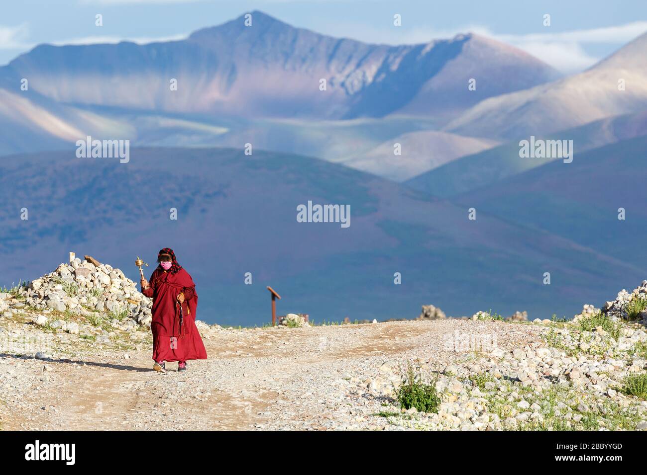 Landschaft des Tibetischen Plateau mit Bergkette. Im Vordergrund eine buddhistische Pilgerin mit einem Handgebetsrad. In einem roten Gewand gekleidet. Stockfoto