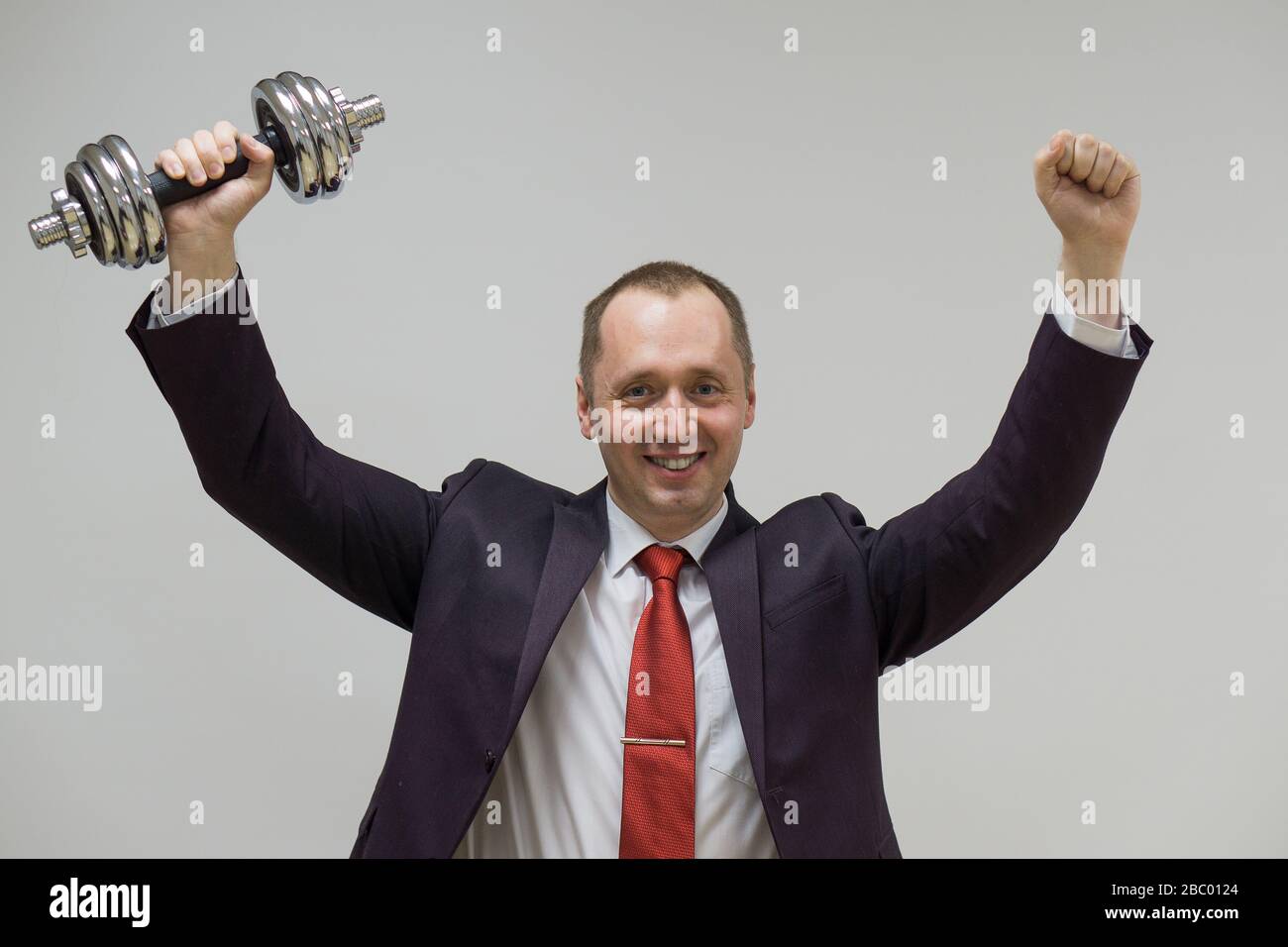 Porträt eines selbstbewussten Geschäftsmannes, der die Hanteln über den hellen Hintergrund hebt. Stockfoto