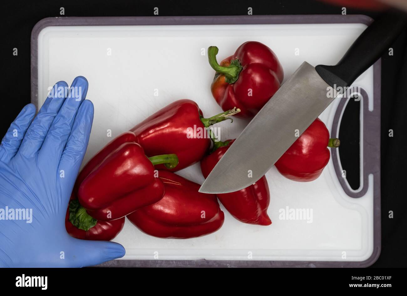 Man in Hygiene Handschuhe schneidet Red Sweet Peppers at Home mit Messer, Vorsorge gegen Corona Virus 2020 Stockfoto