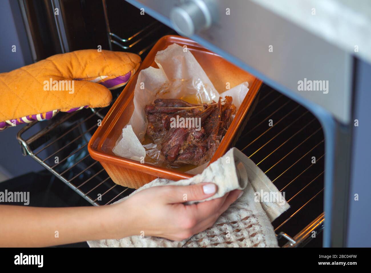 Das Entenfleisch wird im Ofen auf einem keramischen Backblech gebacken. Die Hände eines Mädchens legen das Backen in den Ofen. Stockfoto