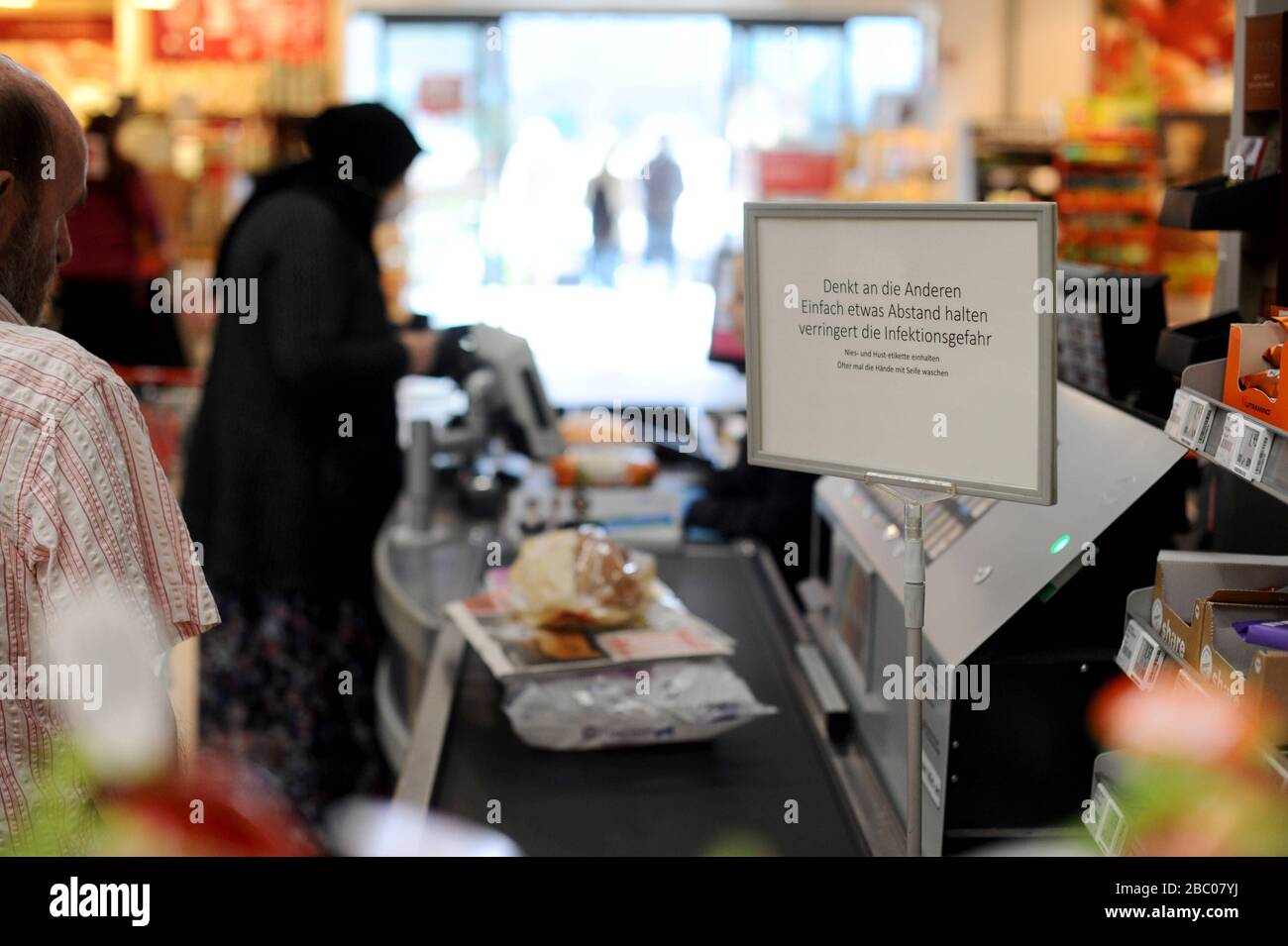 Lebensmitteleinkäufe in Zeiten der Corona-Pandemie: Im Bild ein Kassierer mit Schutzhandschuhen bei der Arbeit in einer Filiale der Supermarktkette Rewe in Obergiesing. Schilder bitten die Kunden, ihre Distanz zu halten, während sie warten. [Automatisierte Übersetzung] Stockfoto