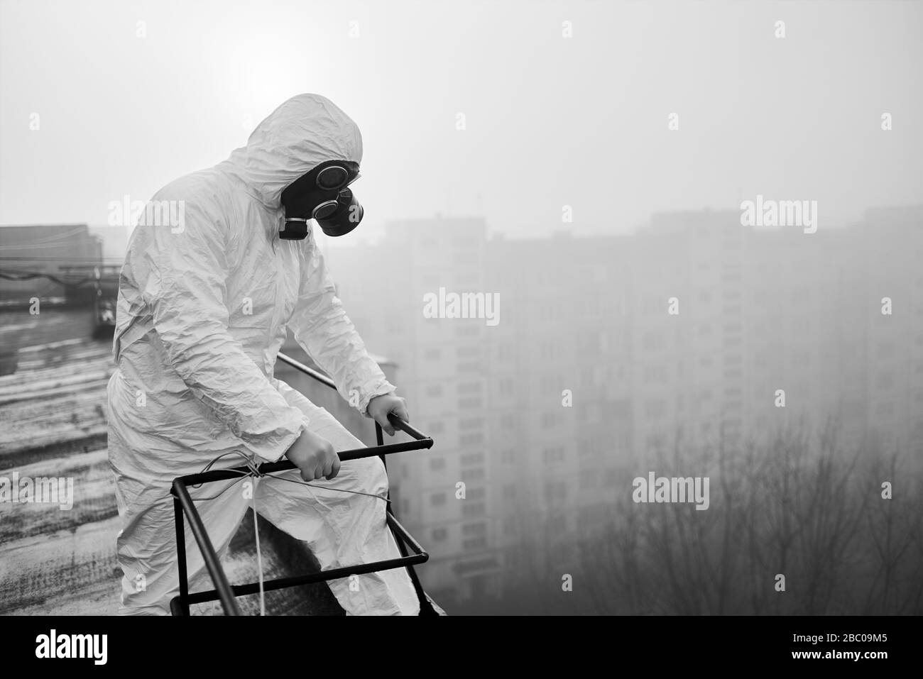 Wissenschaftler, der Schutzkleidung und Gasmaske trägt und auf dem Dach steht, erkundet das Gebiet seiner potenziellen Studie über gefährliche Emissionen in die Atmosphäre. Schwarz-Weiß-Bild Stockfoto
