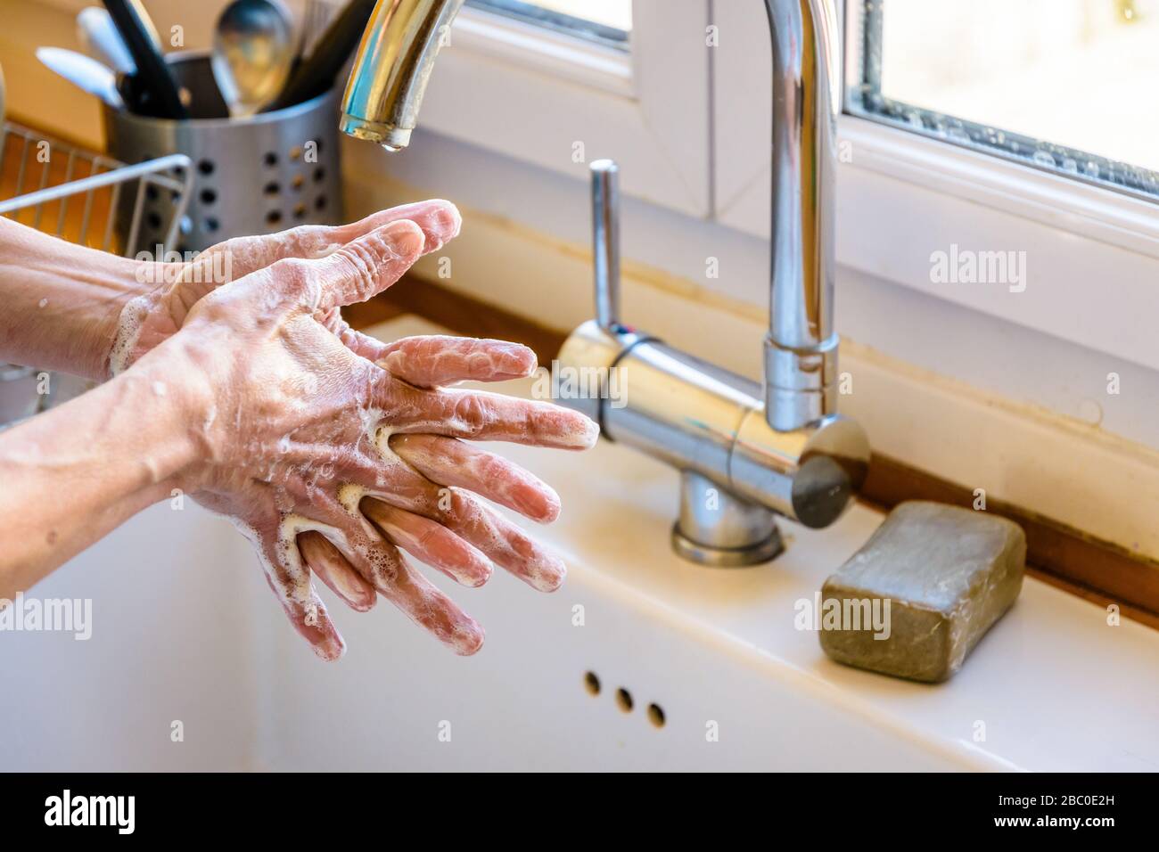 Nahaufnahme der Hände einer Frau, die ihre Hände gründlich mit Seife unter dem Hahn der Küchenspüle waschen. Stockfoto