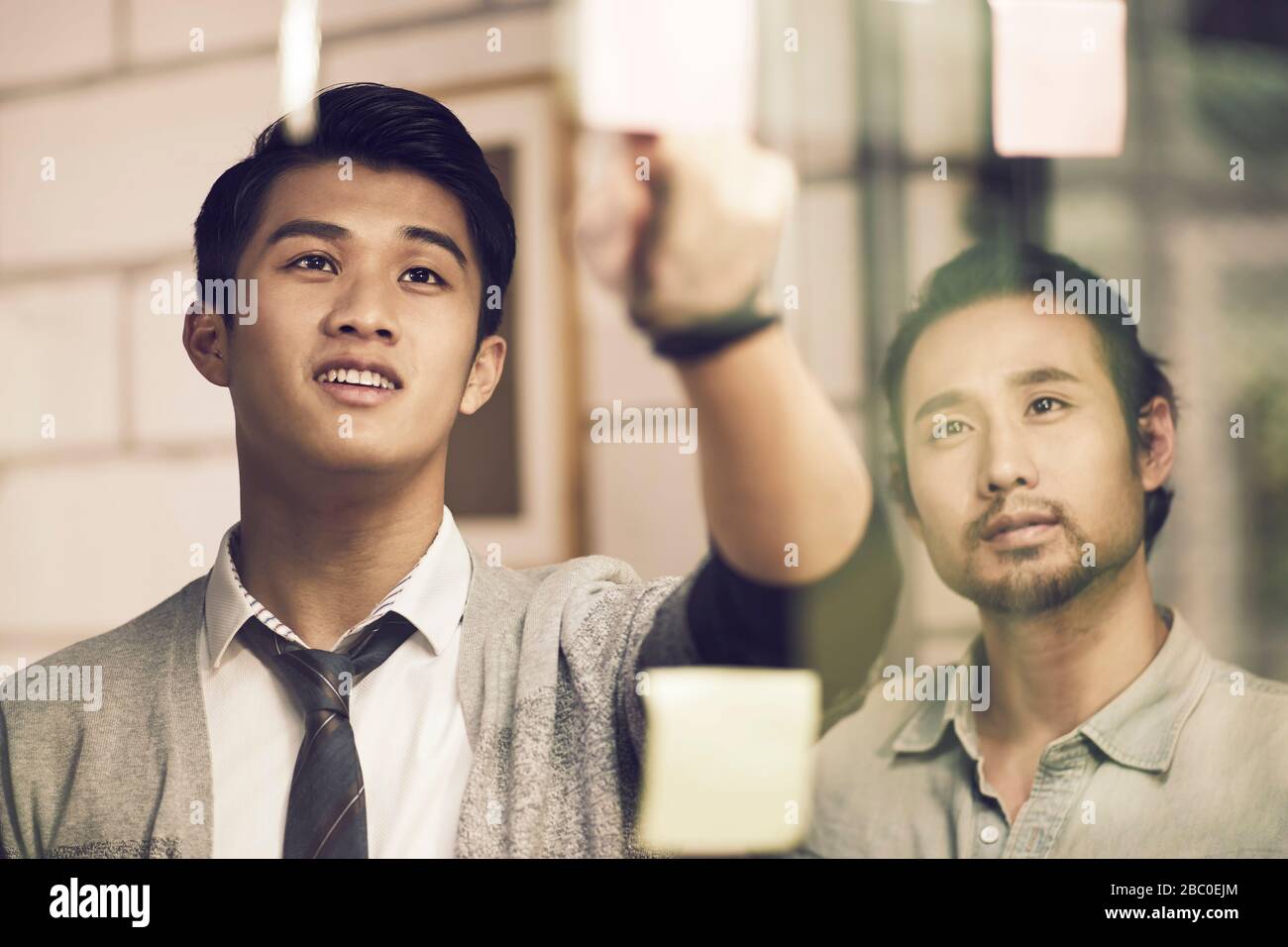 Zwei asiatische Kleinunternehmer junge Unternehmer, die mit Haftnotizen im Büro diskutieren Stockfoto
