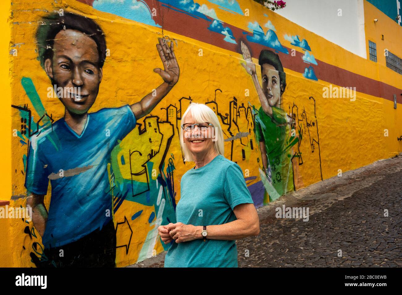 Südafrika, Kapstadt, Schotsche Knoof, Bo Kaap, Wale St, hochrangiger weiblicher Tourist posierte vor Graffiti-Futter steiler gepflasterter Gasse Stockfoto