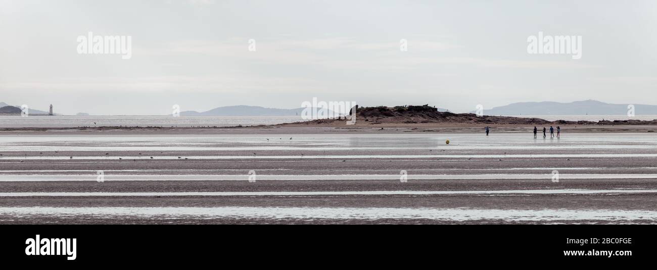 Little Eye Island bei Ebbe, die kleinste der Hilbre Islands, mit dem Punkt des Ayr Leuchtturm in Nordwales in der Ferne sichtbar. Stockfoto