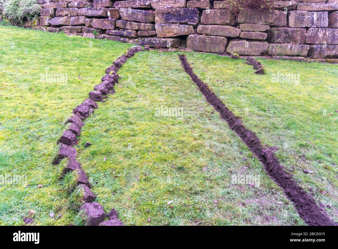 Installation eines Ablaufgrabens in einem Gartenrasen, Stockfoto