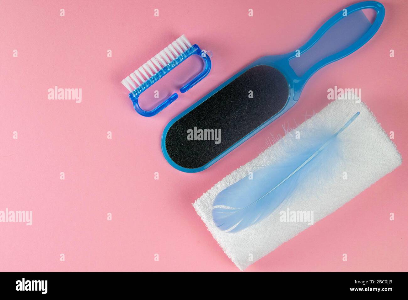 Das Konzept der schönen und gesunden Füße. Pedikürbürste, Fußstein und weiße Handtücher mit blauem Stift auf pinkfarbenem Hintergrund. Draufsichten mit klarem Raum Stockfoto