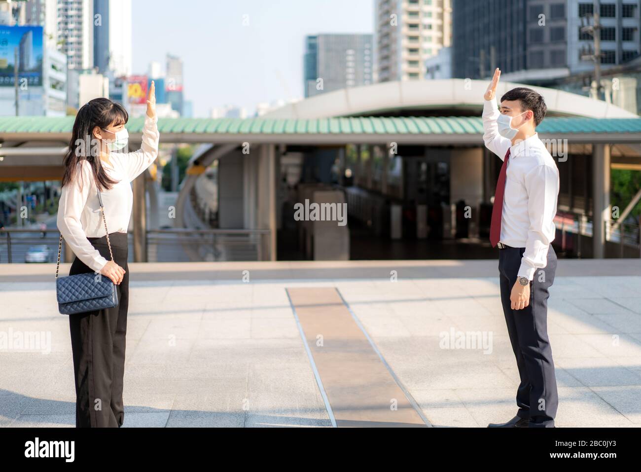 Der asiatische Wirtschaftsmann und die asiatische Frau grüßen und sagen Hallo mit der Geschäftskollegin und tragen Maske Stehabstand von 1 Meter Abstand Schutz vor COVID-19 Stockfoto
