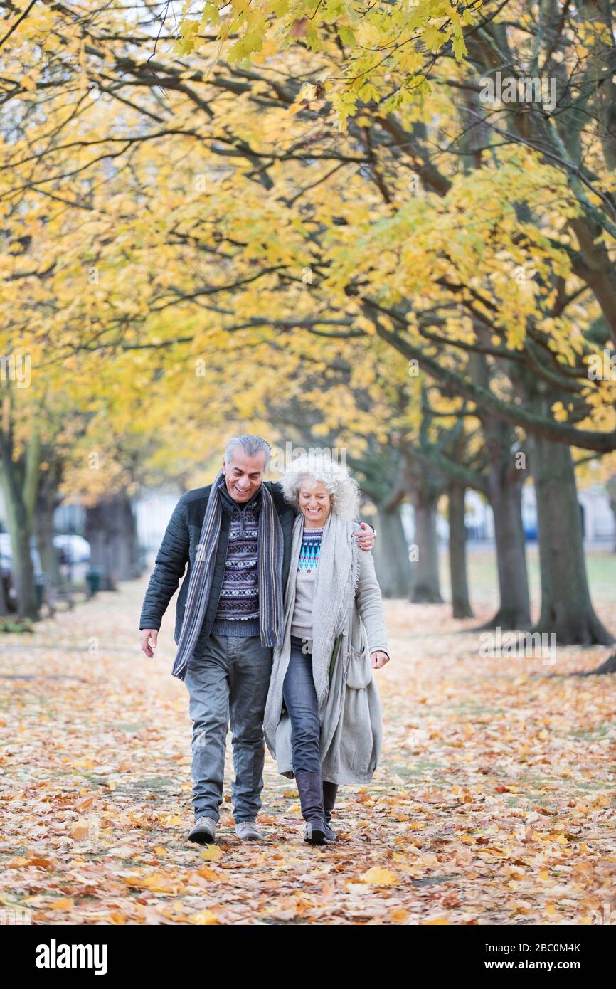 Liebevolles Senioren-Paar, das im Herbstpark zwischen Stress und Blättern spaziert Stockfoto