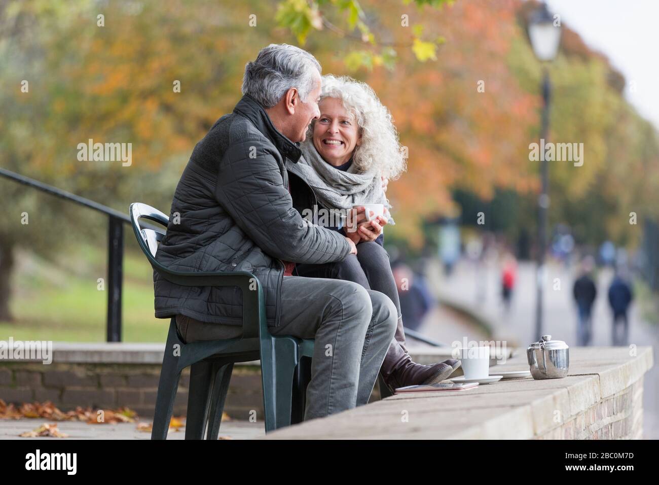 Lächelndes, liebevoll aktives Senioren-Paar, das im Herbstpark Tee trinkt Stockfoto