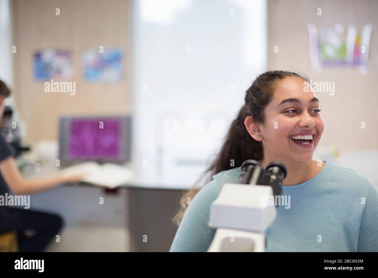 Lachende Studentin am Mikroskop im Laborunterricht Stockfoto