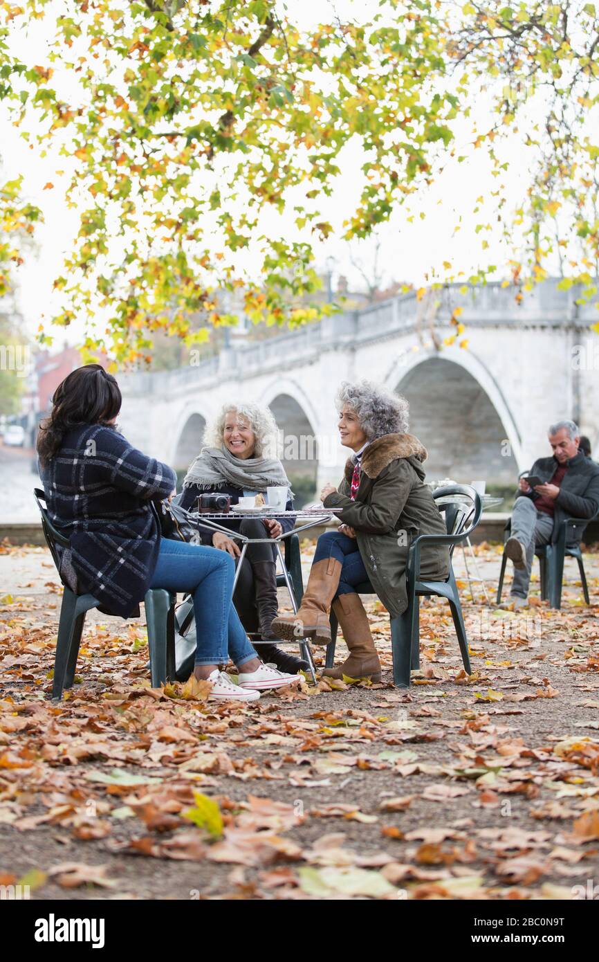 Lächelnde aktive Senioren-Freunde, die im Café des Herbstparks Kaffee genießen Stockfoto