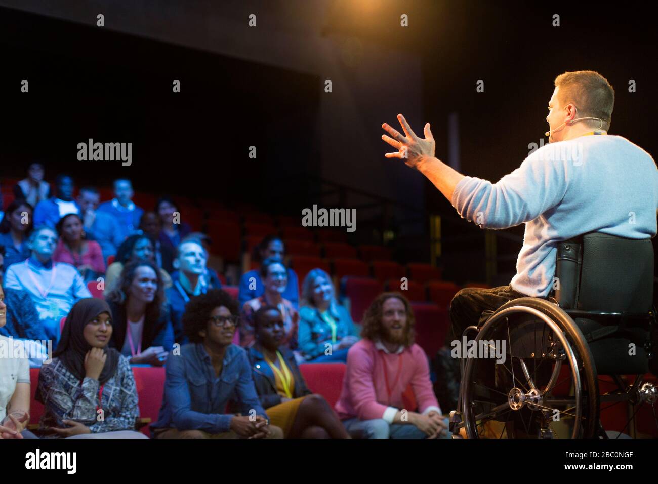 Sprecher im Rollstuhl auf der Bühne spricht mit Konferenzpublikum Stockfoto