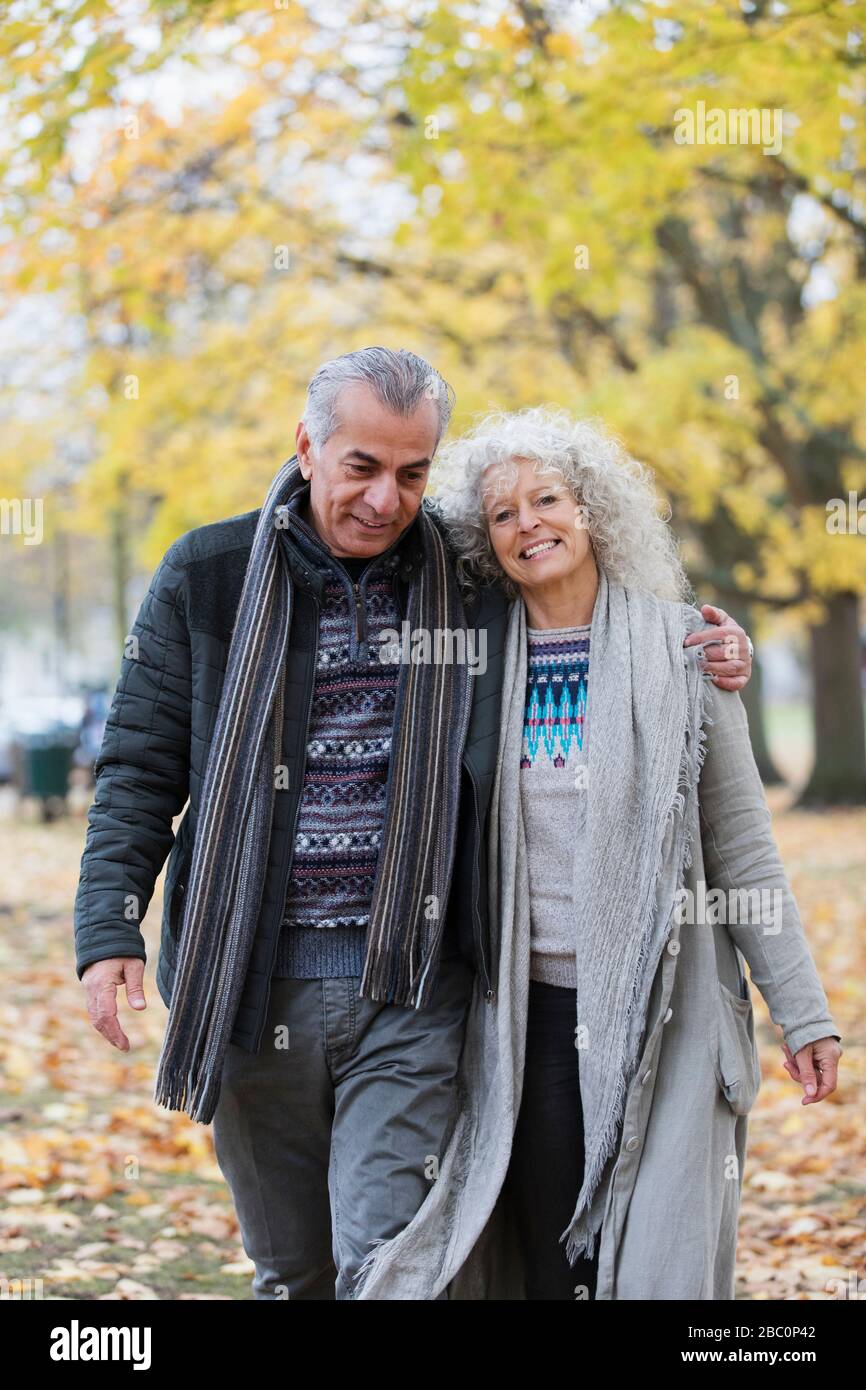 Selbstbewusstes, lächelndes Senioren-Paar, das umarmt und im Herbstpark spaziert Stockfoto