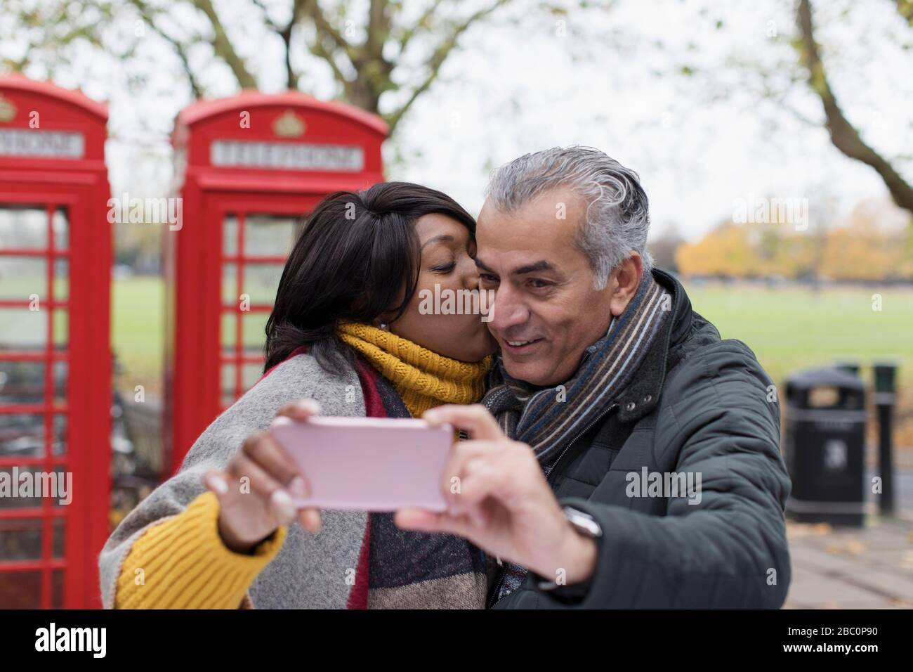 Senioren-Paar küsst und nimmt selfie in Park vor roten Telefonzellen Stockfoto