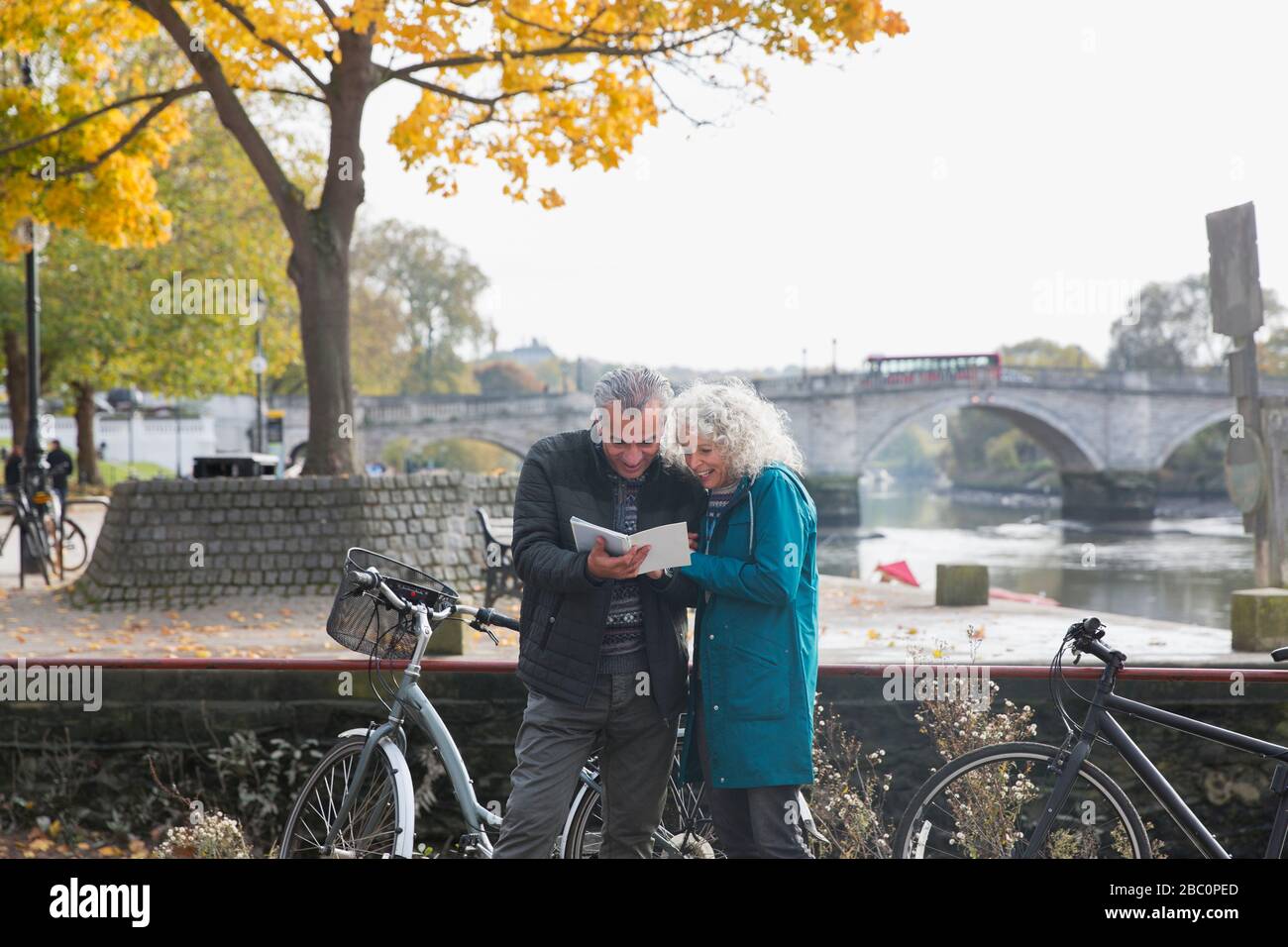 Älteres Paar mit Fahrrädern, mit Blick auf den Reiseführer entlang des Herbstflusses Stockfoto