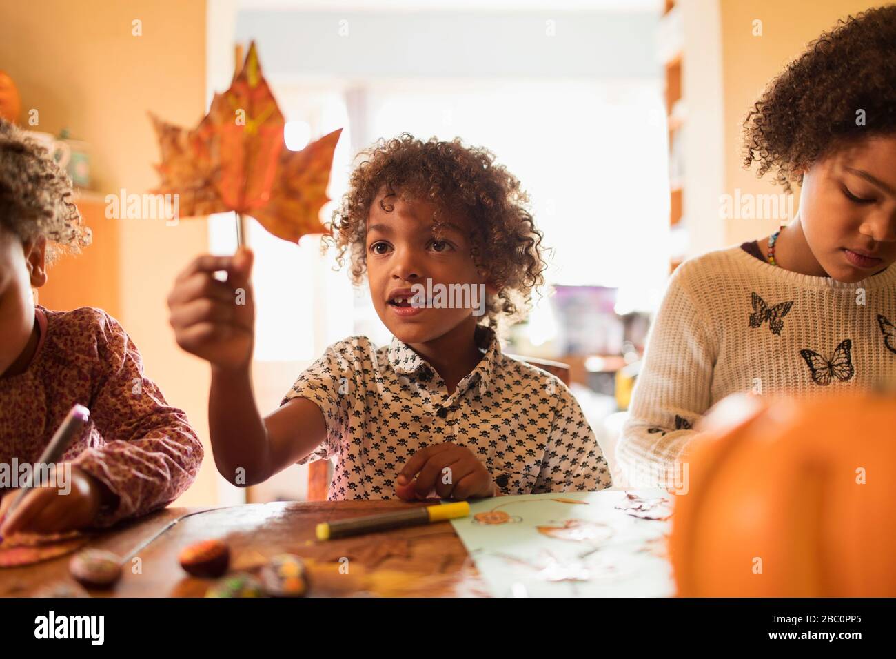 Neugieriger Junge, der das Herbstblatt am Tisch hält Stockfoto