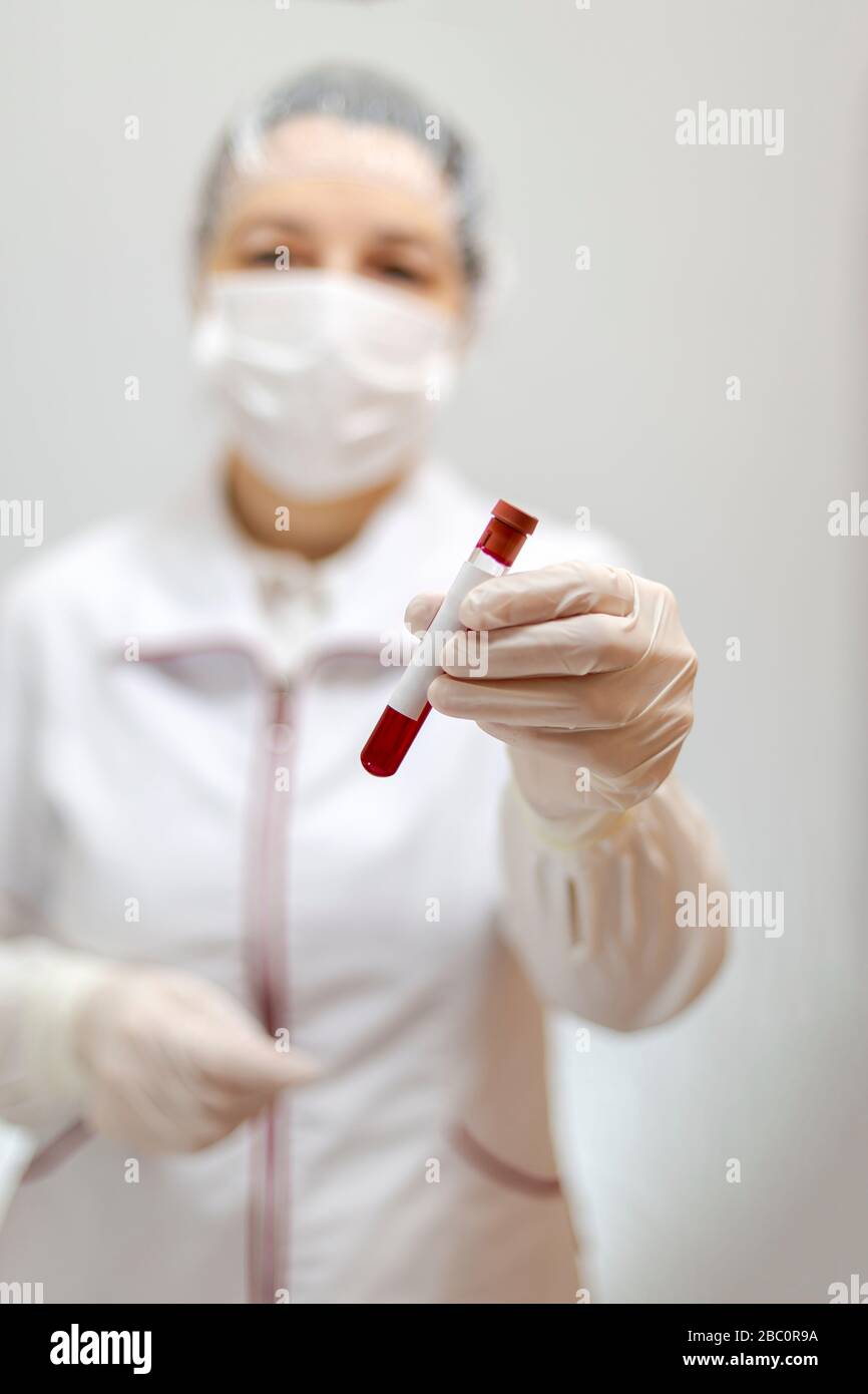Assistent oder Arzt mit Maske und Handschuhen, die ein Rohr mit medizinischer Analyse, Blut und Textstelle enthalten Stockfoto