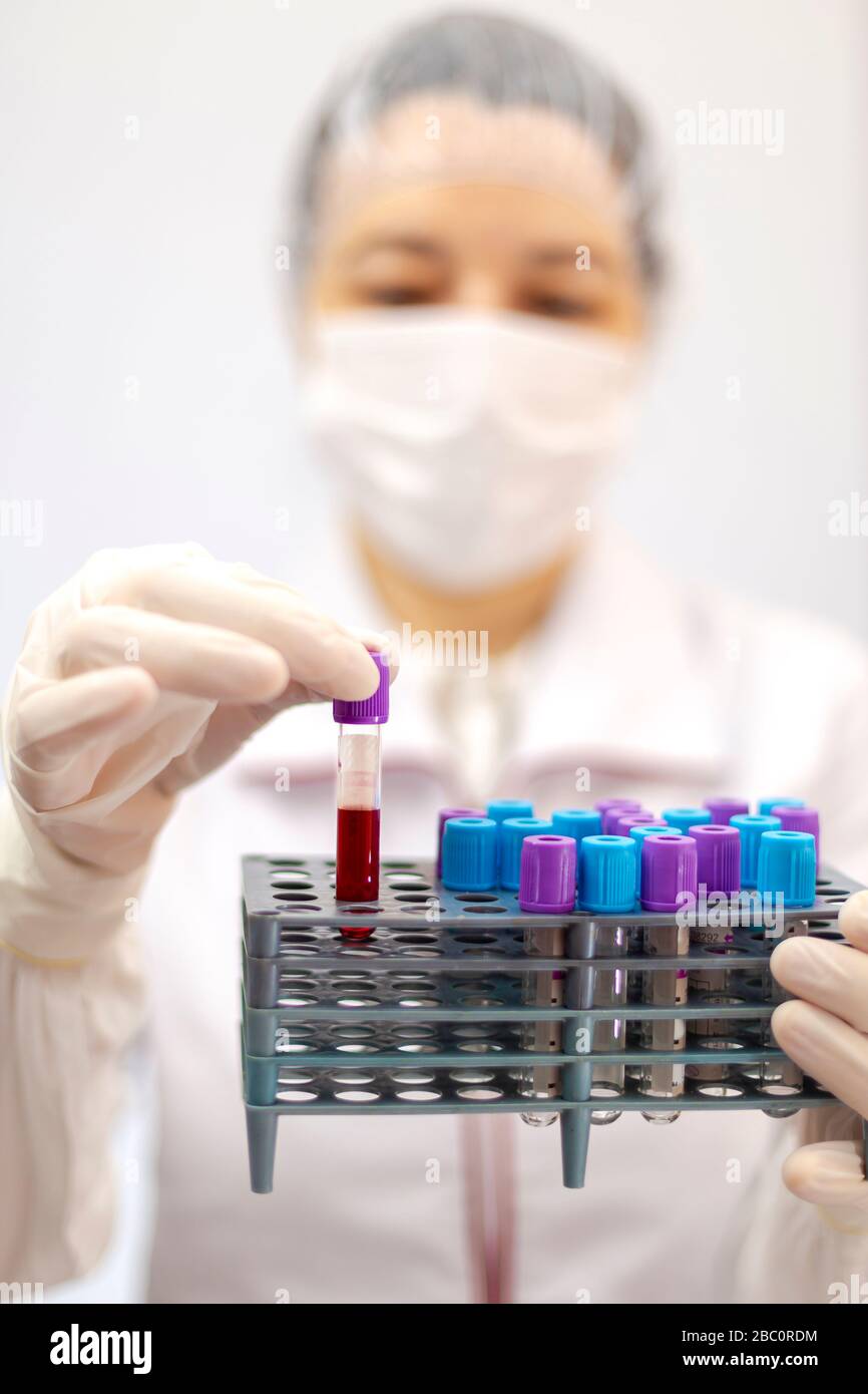 Wissenschaftler, Krankenschwester oder Arzt mit Maske und Handschuhen, die einen Rechen von Röhrchen mit medizinischer Analyse, Blod, Plasma halten. Chemische Analysemethoden. Stockfoto