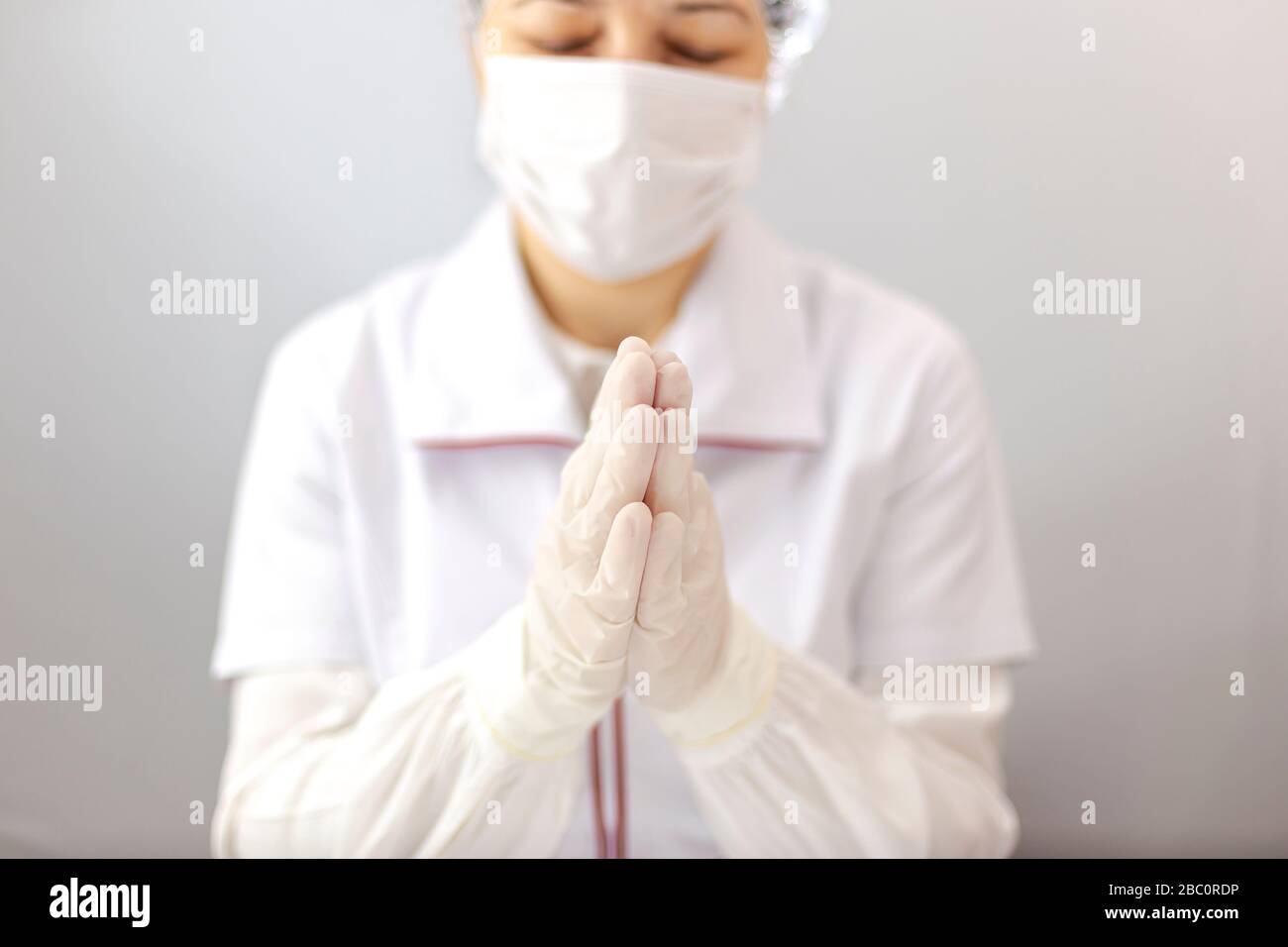 Der Assistent oder Arzt mit Maske und Handschuhen steht im Gebet zu allmächtigem Gott. Arzt mit Schutzausrüstung, der Geste des Betens macht Stockfoto