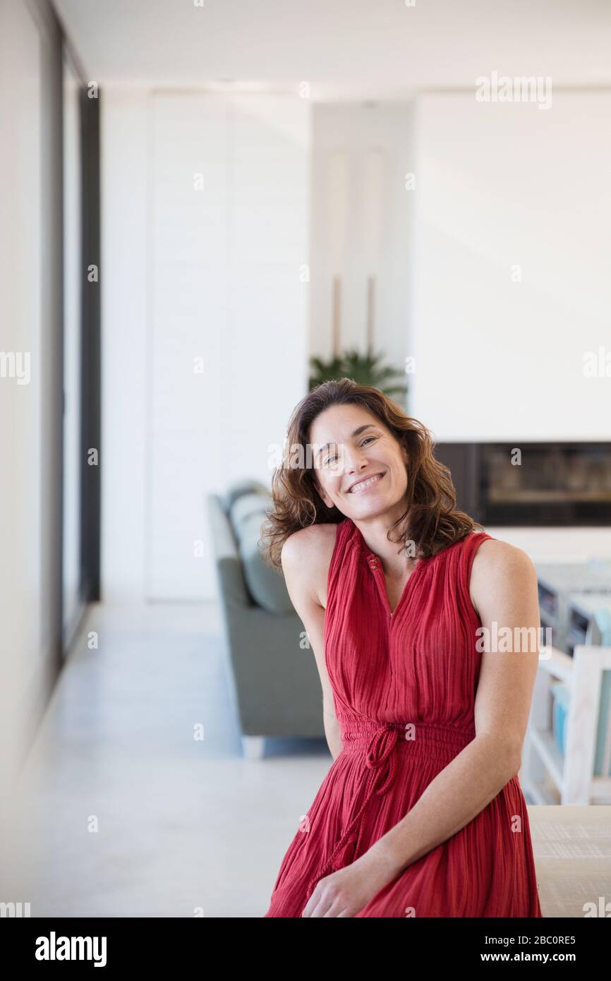 Portrait lächelnde, selbstbewusste brünette Frau in rotem Kleid zu Hause Stockfoto