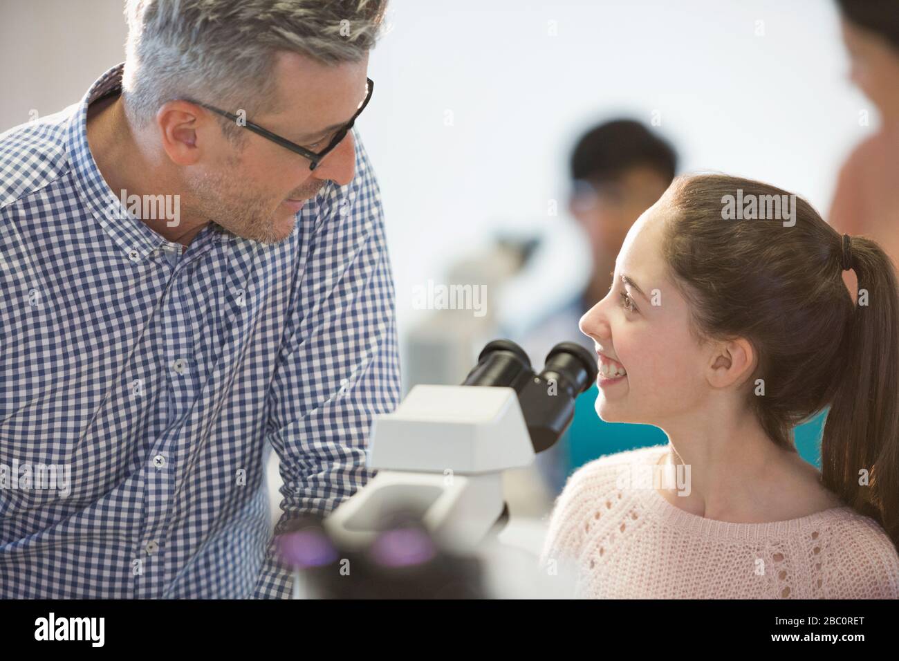 Männliche Lehrerin und lächelnde Schülerin, die wissenschaftliche Experimente am Mikroskop im Laborunterricht durchführt Stockfoto