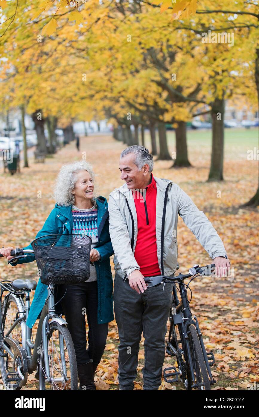 Älteres Paar, das im Herbstpark Fahrräder zwischen Bäumen und Blättern spazieren geht Stockfoto