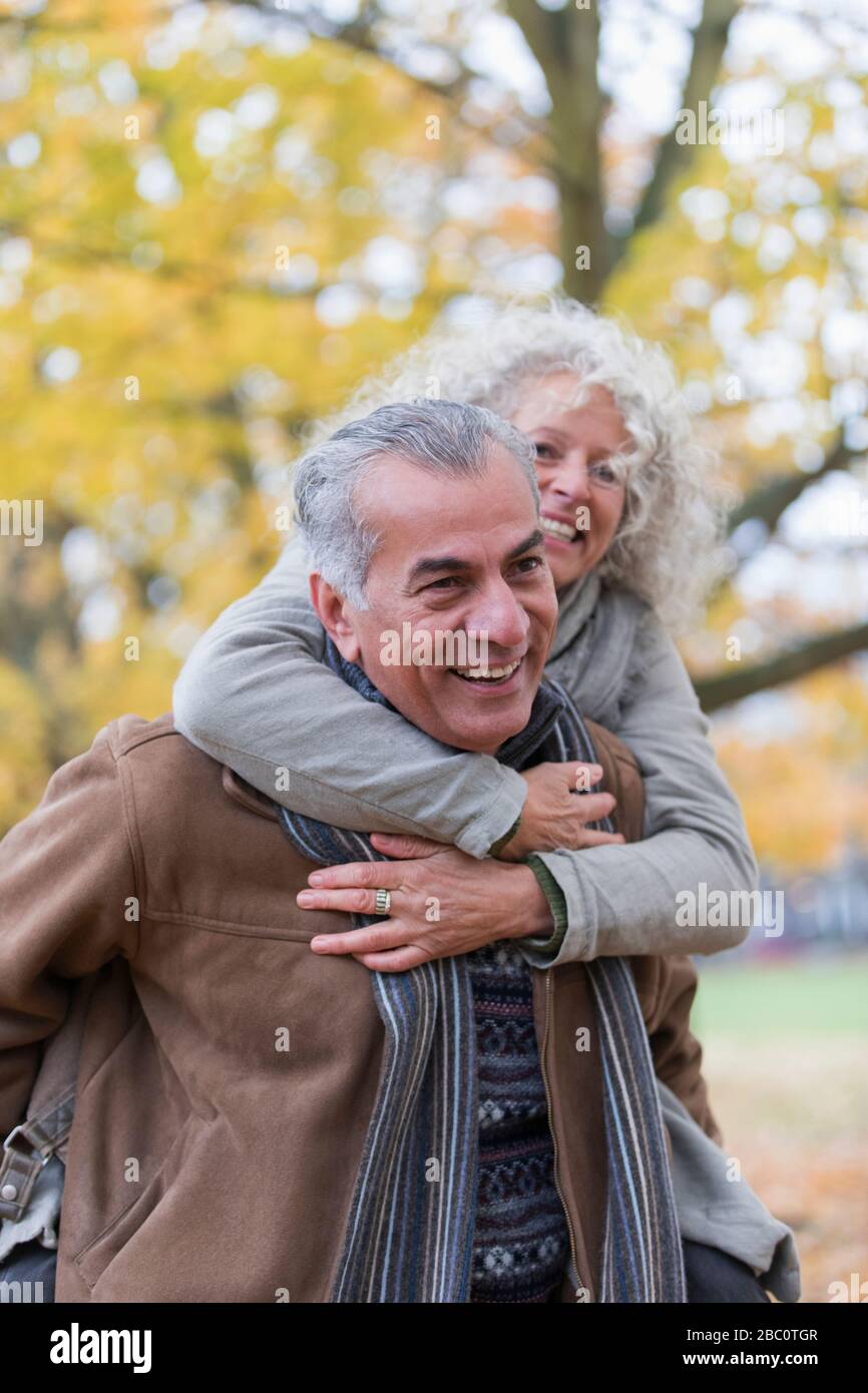 Verspieltes, lächelndes Senioren-Paar piggybacking im Herbstpark Stockfoto