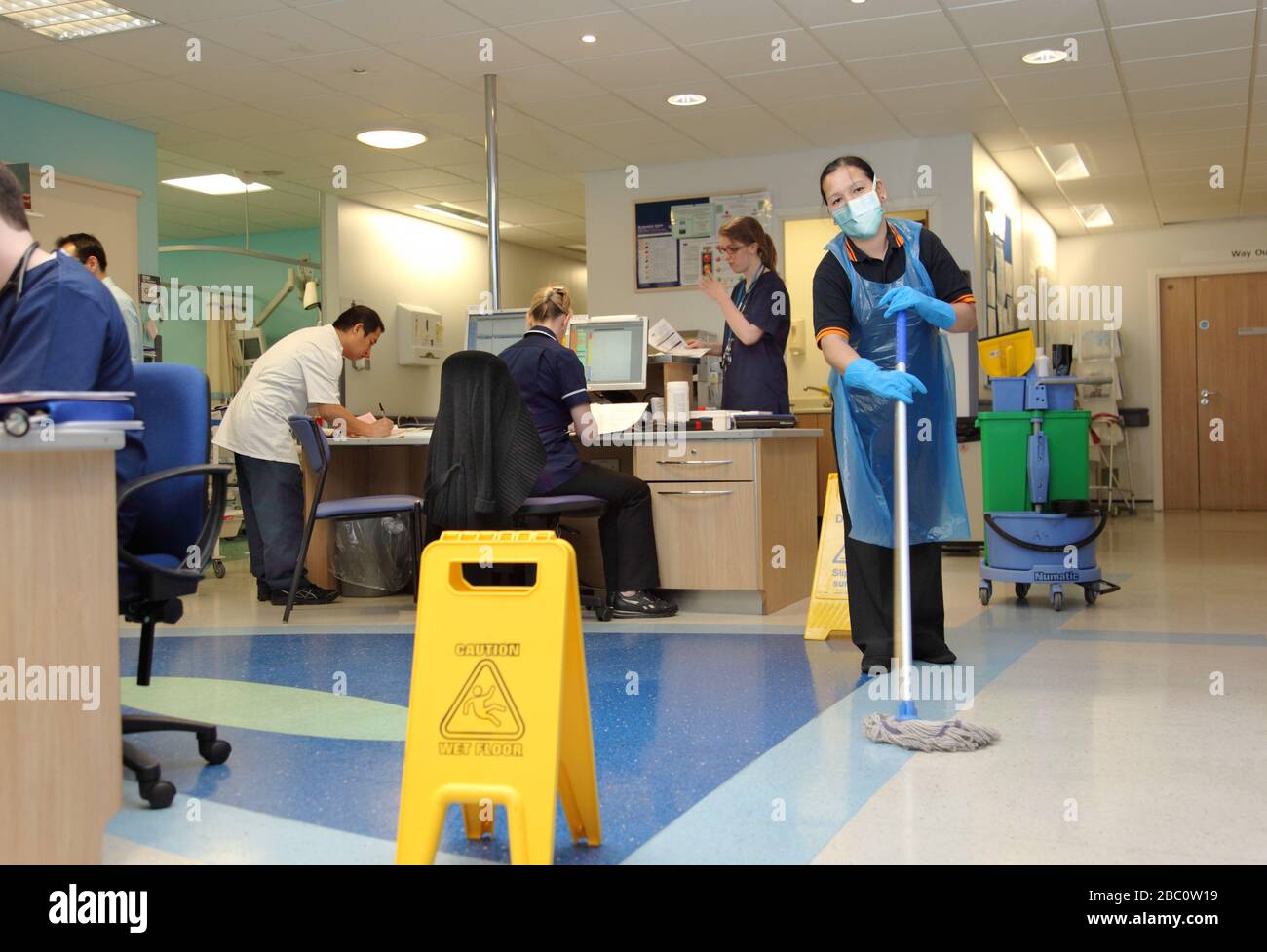Ein Krankenhausreiniger trägt eine schützende Gesichtsmaske, während sie den Boden eines geschäftigen Londoner Krankenhauses ward.UK reinigt Stockfoto