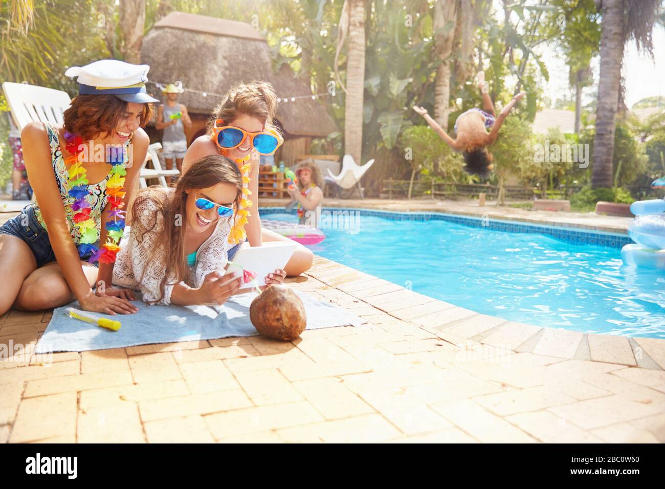 Junge weibliche Freunde hängen am sonnigen Sommerpool mit einem digitalen Tablet aus Stockfoto