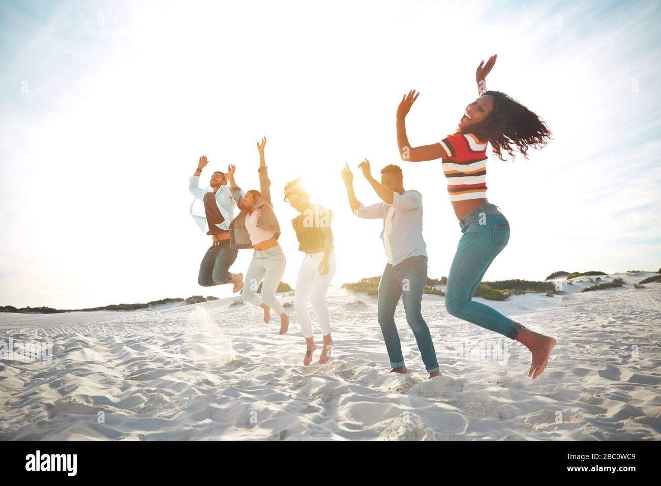 Portrait verspielte, energische junge Freunde springen vor Freude am sonnigen Sommerstrand Stockfoto