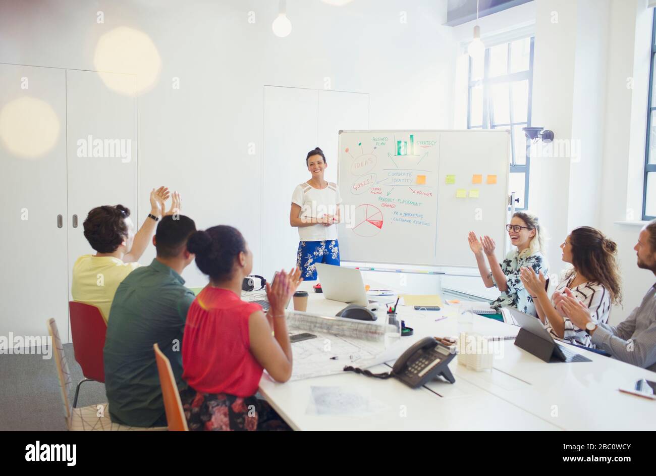 Unterstützende Kollegen klatschen für weibliche Architektin, die das Treffen am Whiteboard leitet Stockfoto