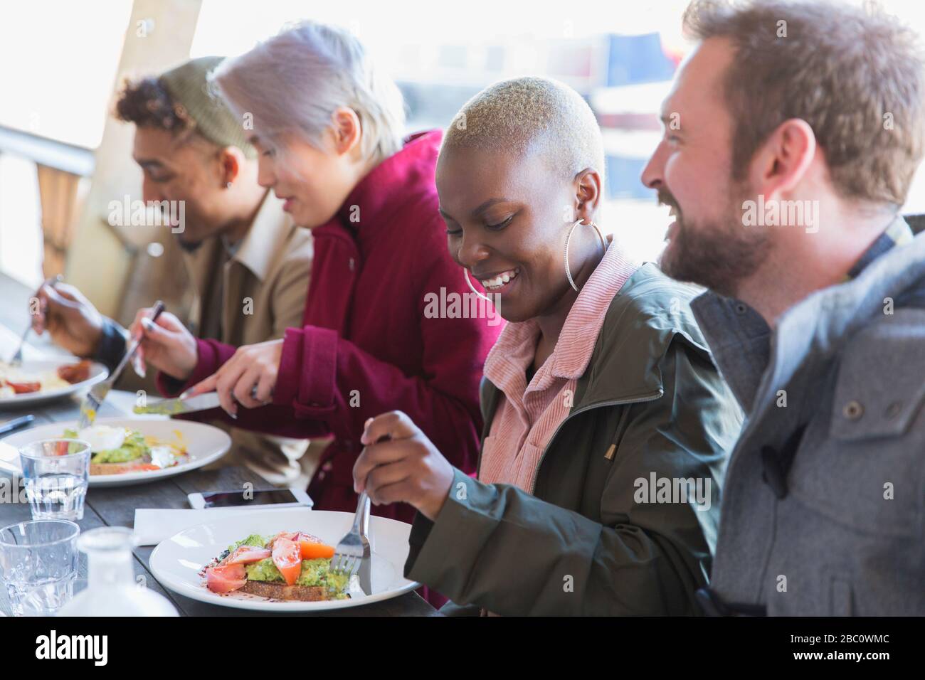Lächelnde junge Frau, die mit Freunden Mittagessen isst Stockfoto
