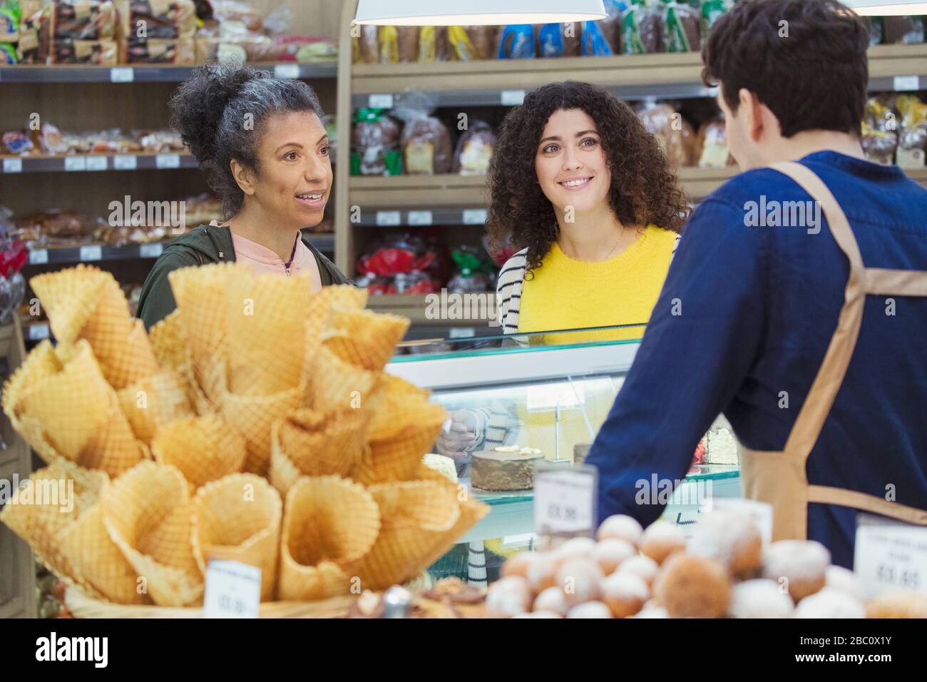 Frauen, die mit Arbeitern in der Vitrine der Bäckerei im Supermarkt sprechen Stockfoto