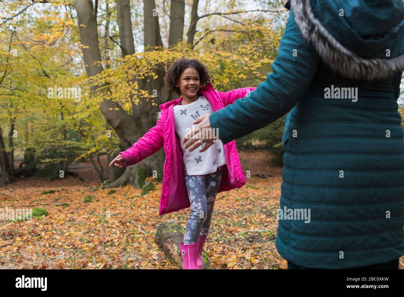Glückliche Mutter und Tochter spielen im Herbstwald auf dem umgefallenen Holzstück Stockfoto