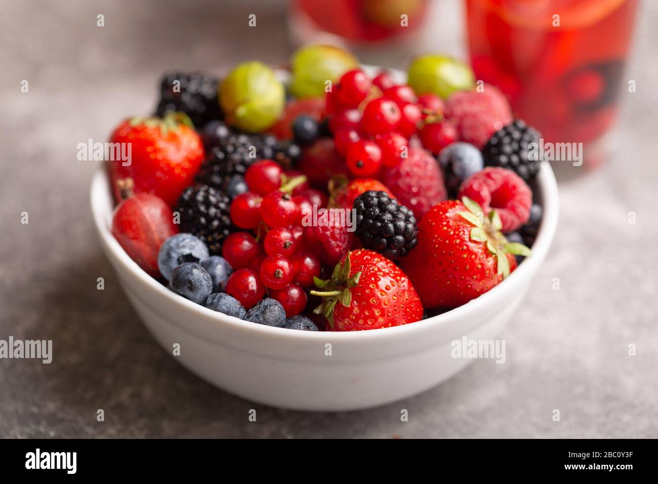 Schale mit frischen Sommerbeeren auf grauem Hintergrund. Stockfoto