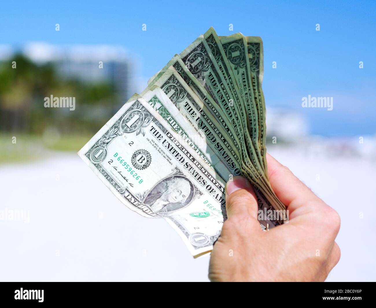 Mann, der US-Dollar-Banknoten hält, Geld in der Hand mit Strandhintergrund. USD-Rechnungen im Konzept von Investitionen, Finanzen und Erfolg im Geschäft. Stockfoto