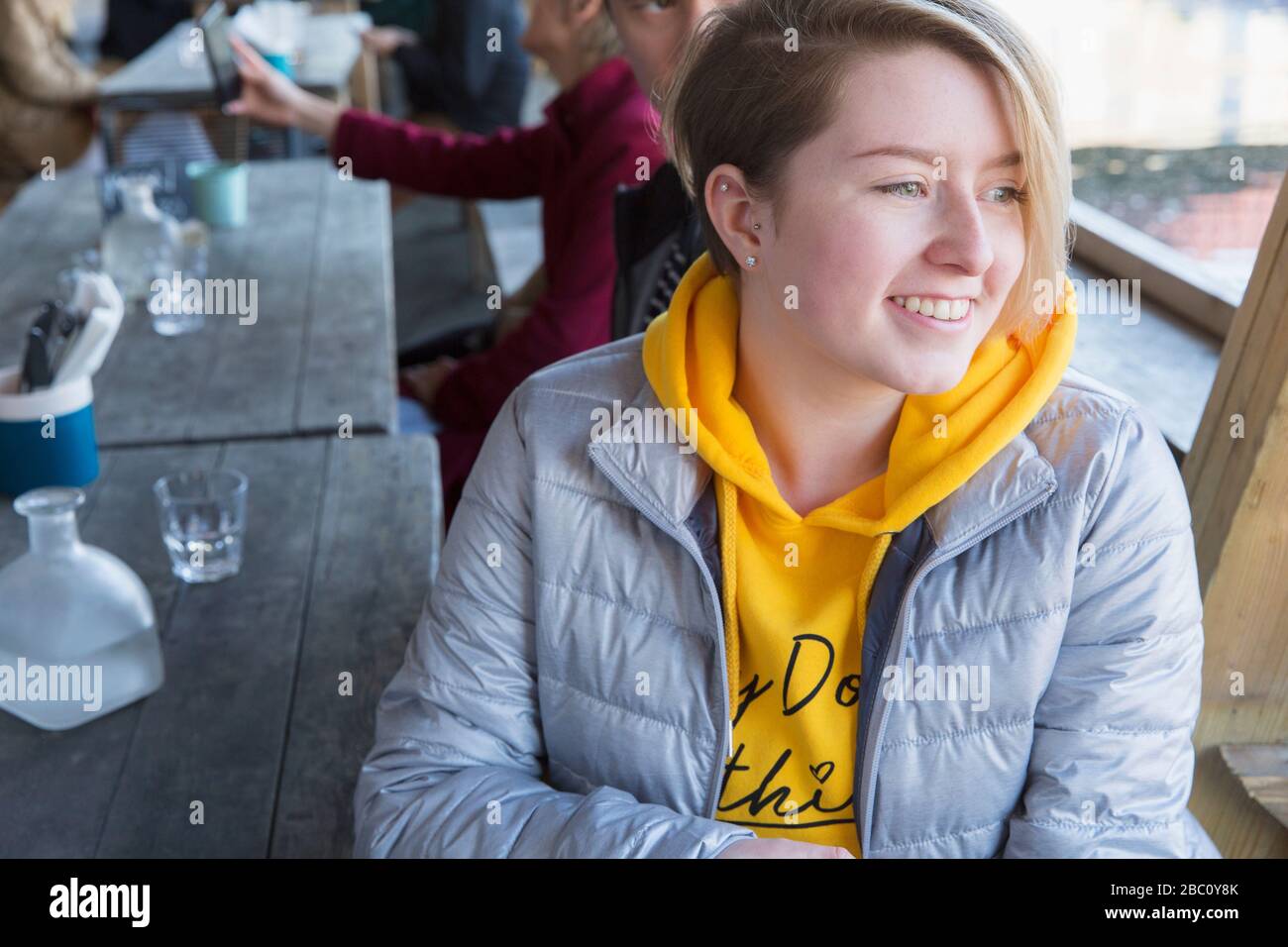 Lächelnde junge Frau, die auf der Terrasse im Restaurant speisen kann Stockfoto